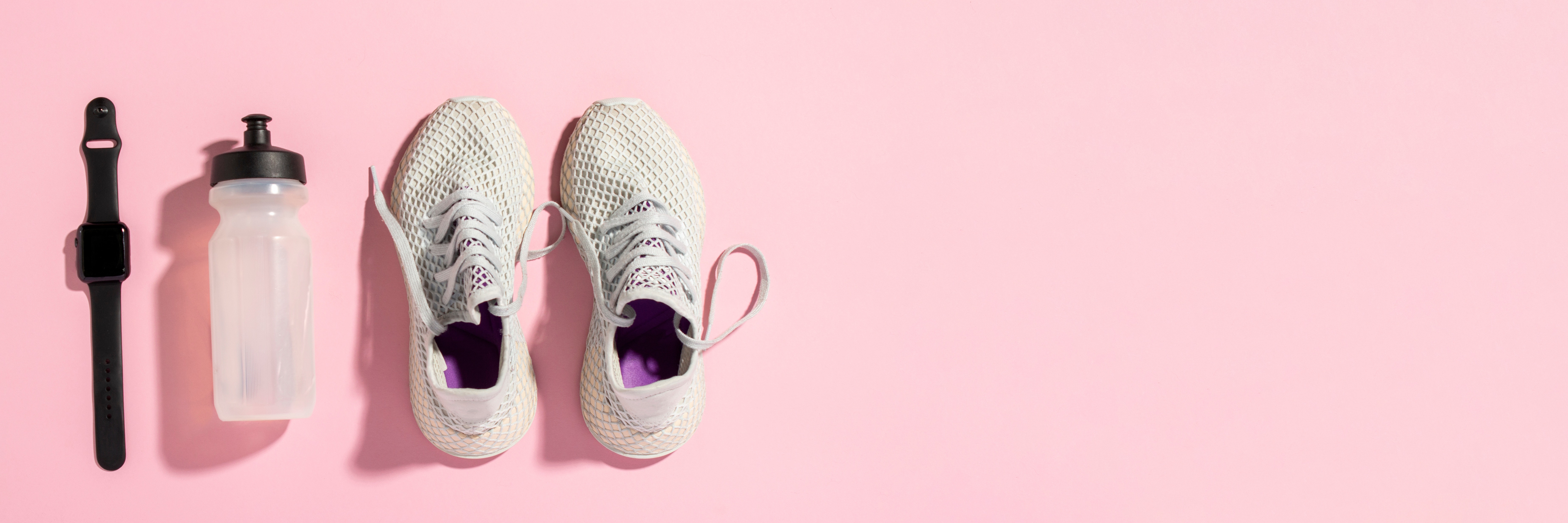 White running shoes, a sports watch and a water bottle on a pink background under the natural light of the morning sun. Concept of jogging, running, hard workout. Banner. Flat lay, top view