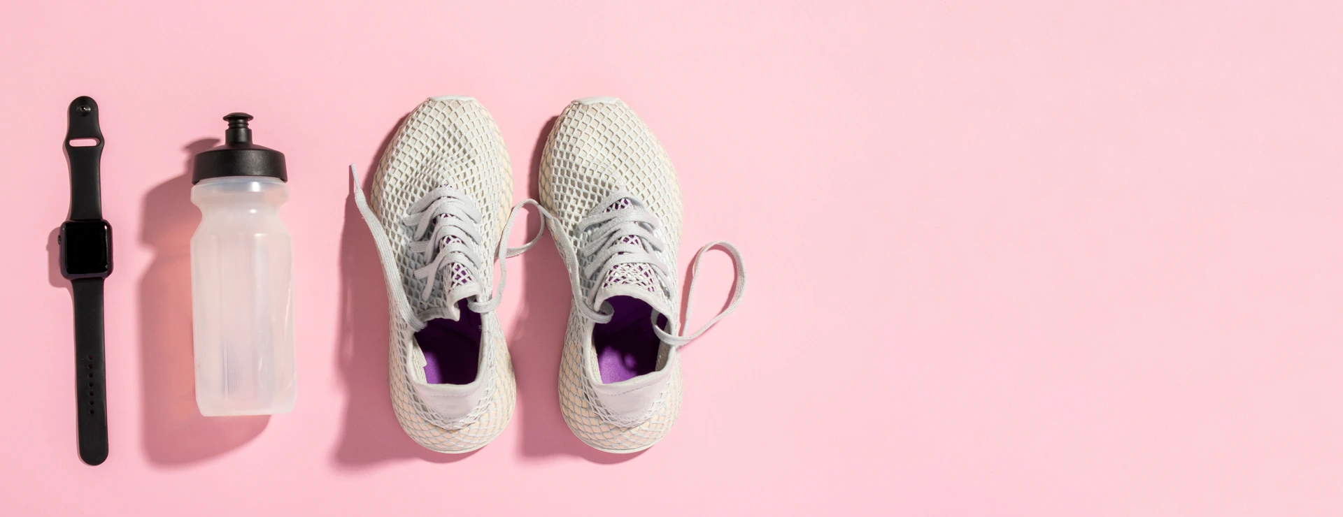 White running shoes, a sports watch and a water bottle on a pink background under the natural light of the morning sun. Concept of jogging, running, hard workout. Banner. Flat lay, top view