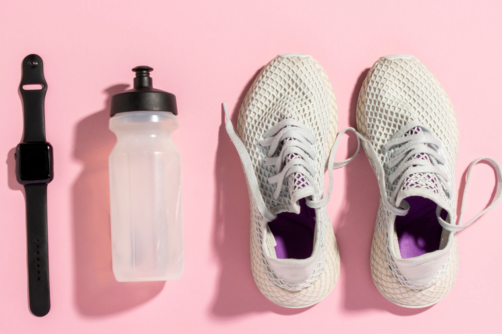 White running shoes, a sports watch and a water bottle on a pink background under the natural light of the morning sun. Concept of jogging, running, hard workout. Banner. Flat lay, top view