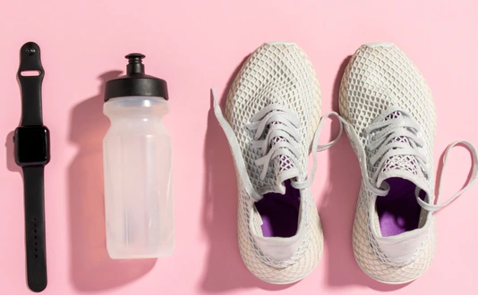 White running shoes, a sports watch and a water bottle on a pink background under the natural light of the morning sun. Concept of jogging, running, hard workout. Banner. Flat lay, top view