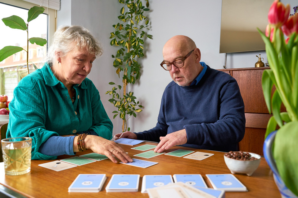 Two elderly people sitting at a table and playing a card game.