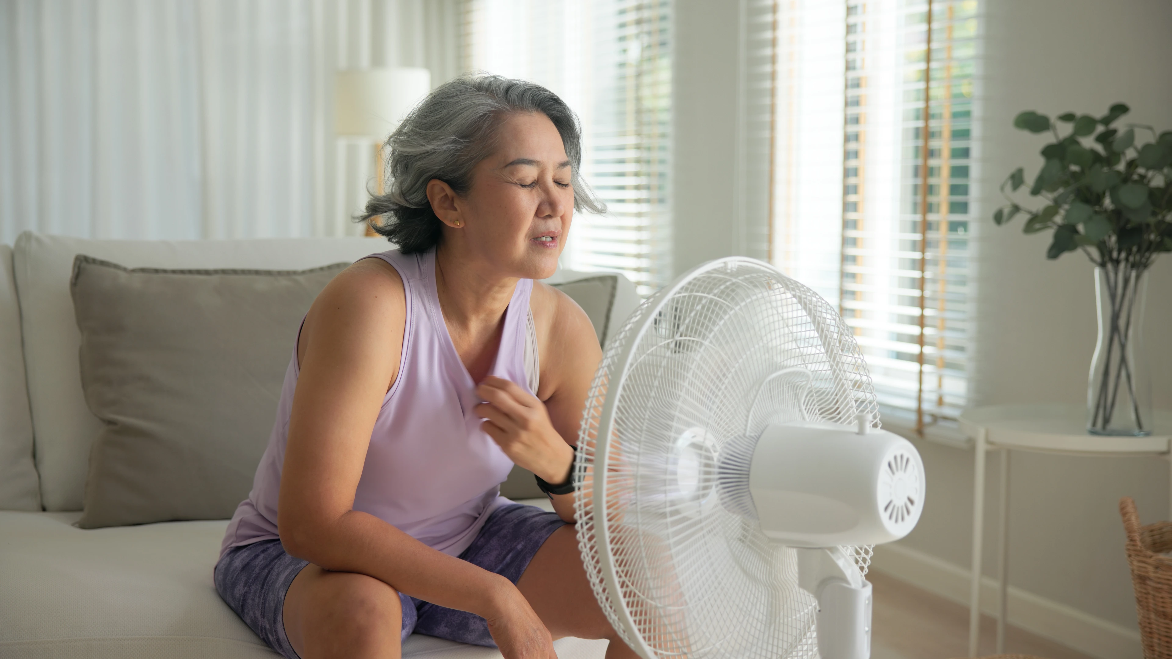 Eine Frau sitzt auf dem Sofa vor einem Ventilator.