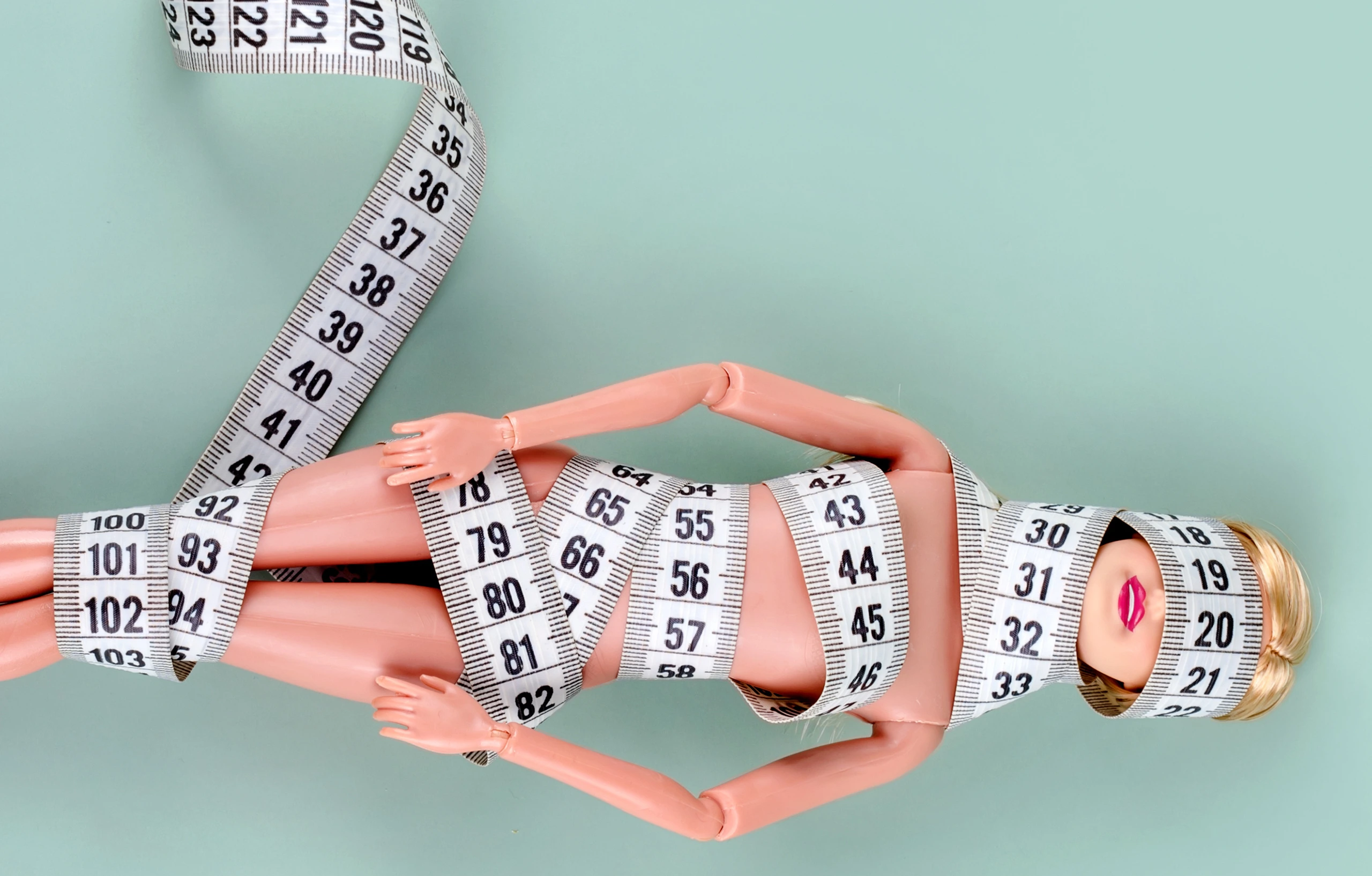 Doll wrapped in measuring tape. Tied up unrecognizable plastic doll, weight loss, fasting and slimming, diet, anorexia, overeating control, female fight for perfect fit body concept. Free copyspace
