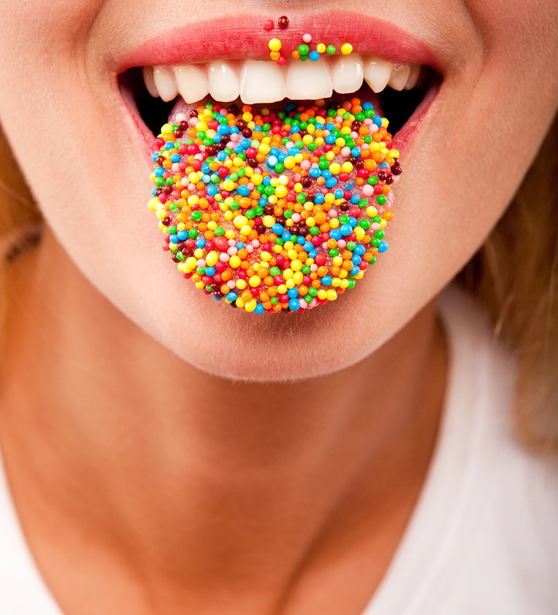 Mund mit ausgestreckter Zunge, die von bunten Zuckerperlen bedeckt ist