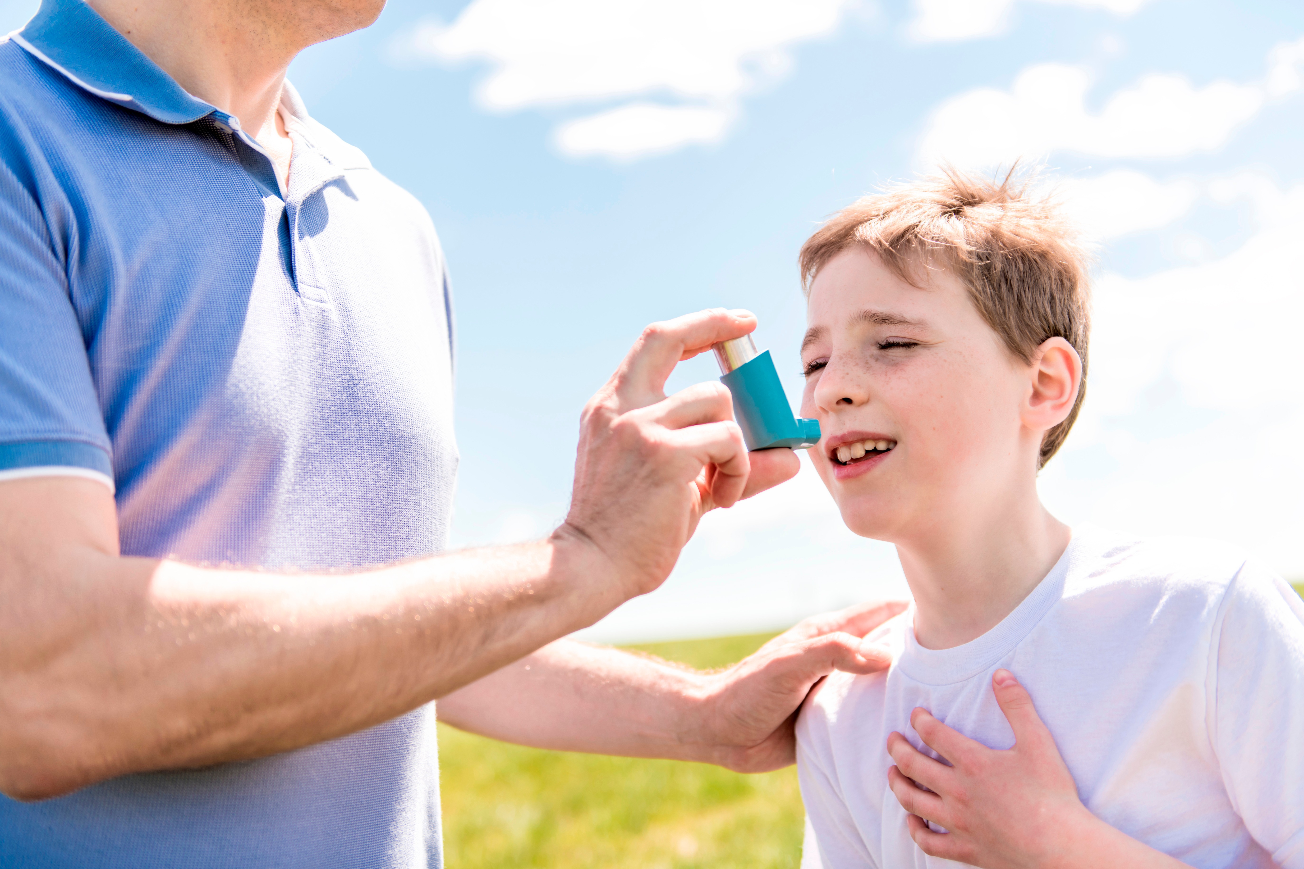 child using inhaler for asthma outside in a park with his father