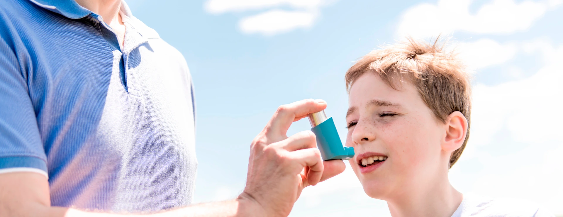 child using inhaler for asthma outside in a park with his father