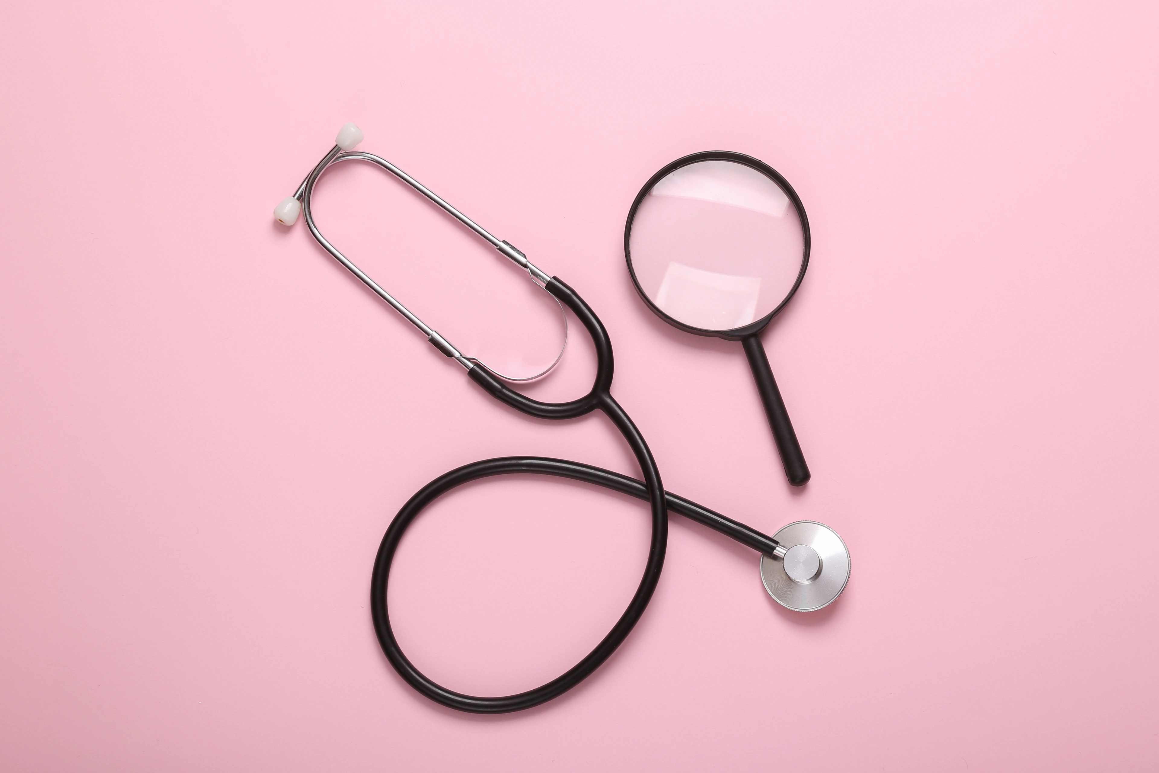 Stethoscope with magnifying glass on pink background. Diagnosis of diseases. Top view