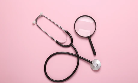 Stethoscope with magnifying glass on pink background. Diagnosis of diseases. Top view