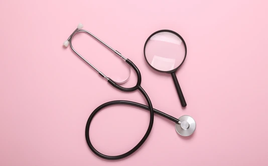 Stethoscope with magnifying glass on pink background. Diagnosis of diseases. Top view