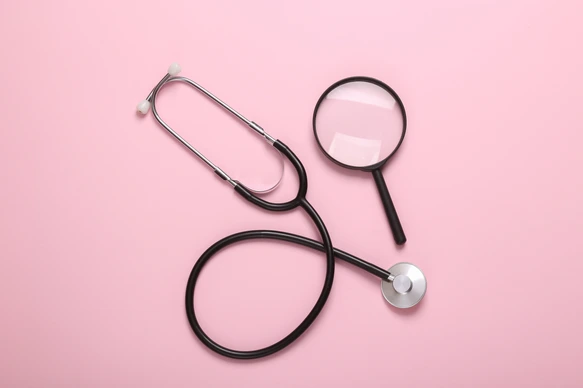 Stethoscope with magnifying glass on pink background. Diagnosis of diseases. Top view