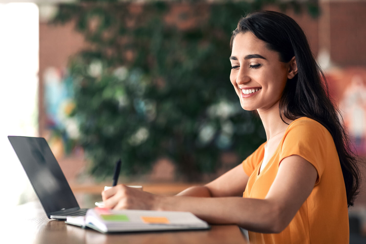 Ein Foto, das eine lächelnde junge Frau zeigt, die vor einem Laptop sitzt