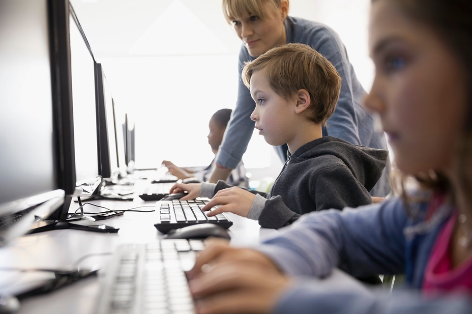 Female teacher helping pre-adolescent boy at computer in classroom