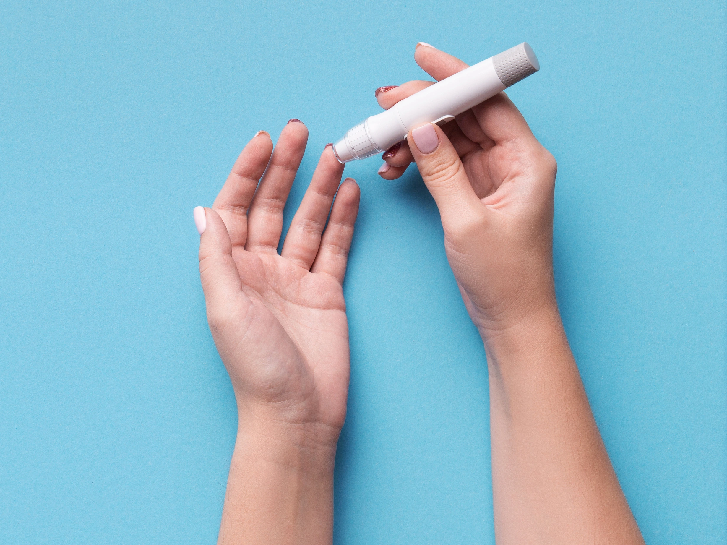 Woman using glucometer on blue background, top view