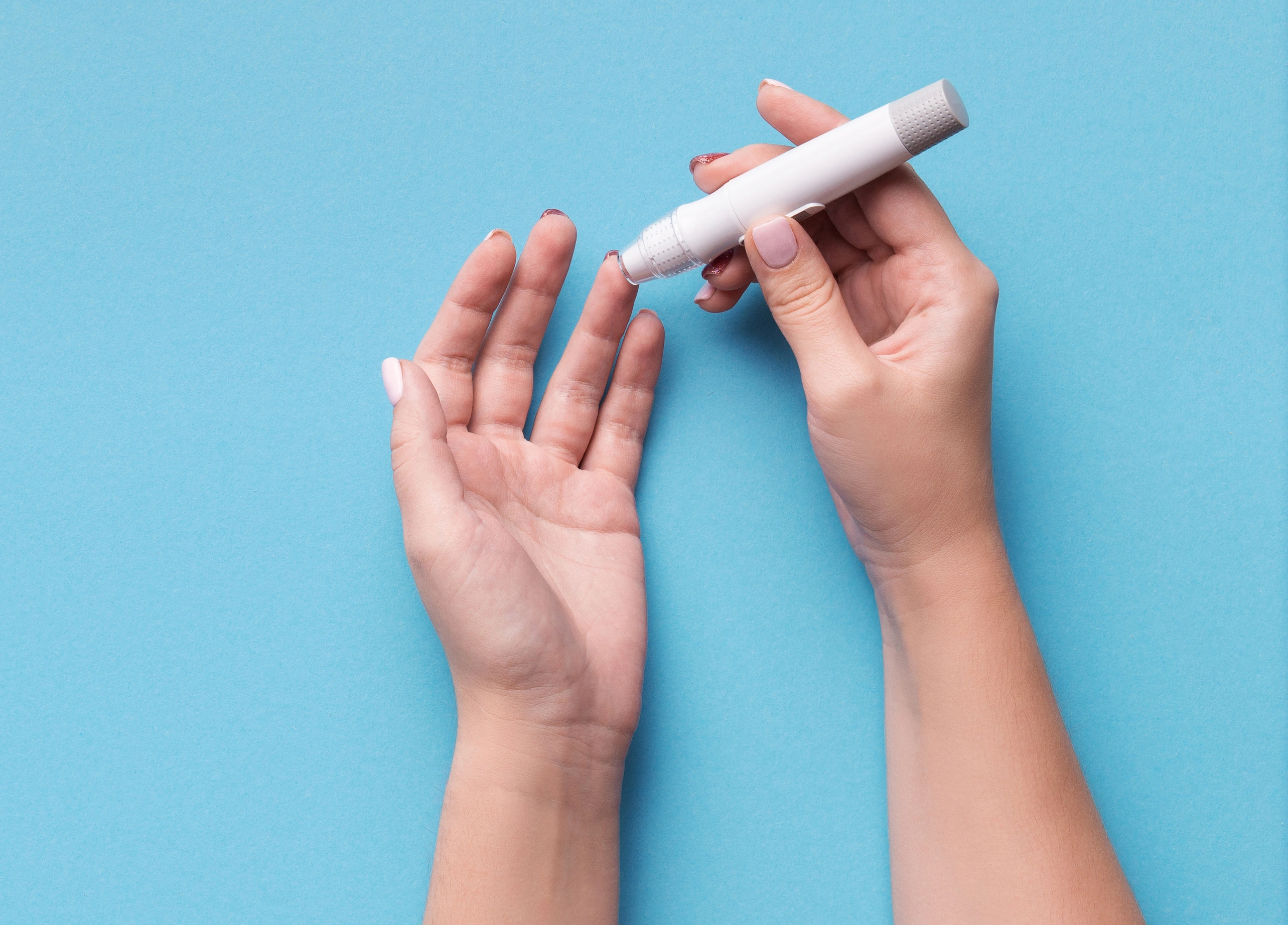 Woman using glucometer on blue background, top view
