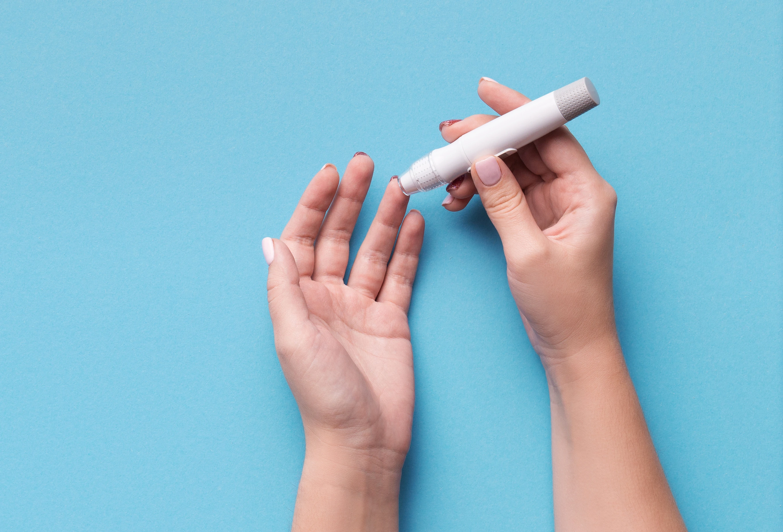 Woman using glucometer on blue background, top view