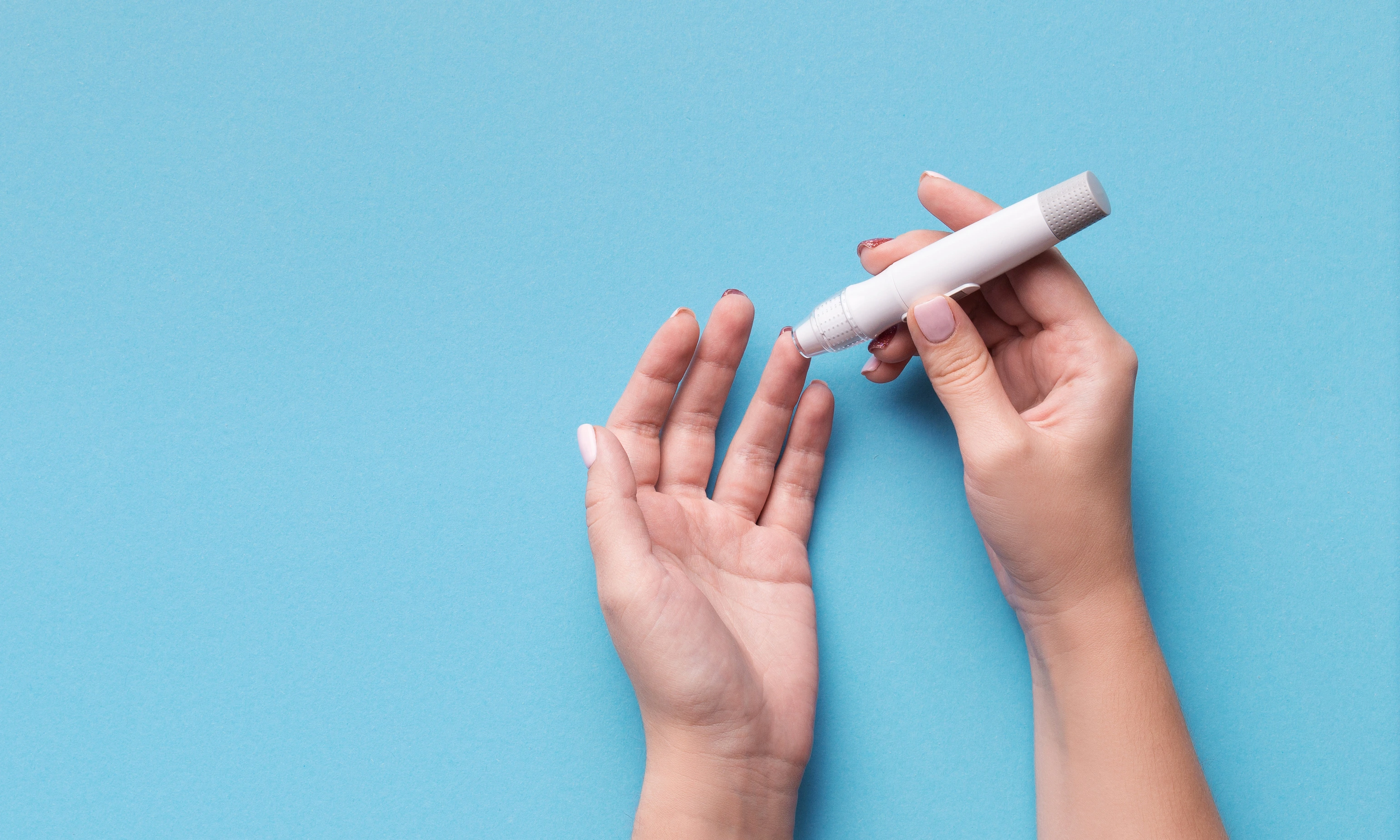 Woman using glucometer on blue background, top view