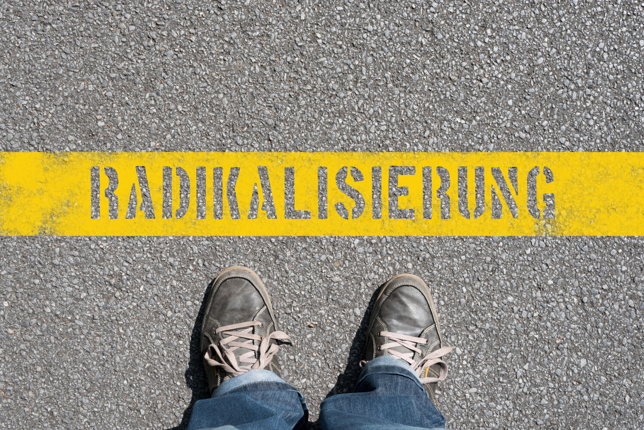 Füße in Schuhen auf einer Straße, die vor der Aufschrift "Radikalisierung" stehen