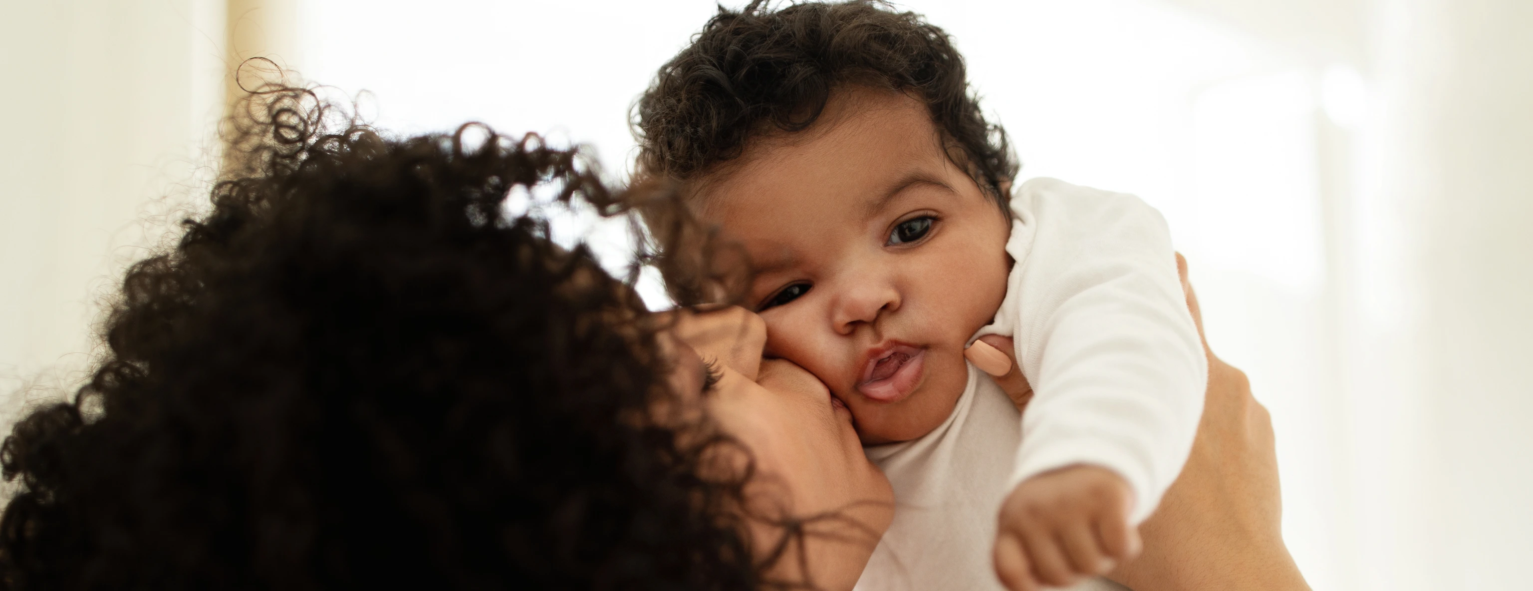 Happy millennial african american mother kissing little child, enjoy relax together, have fun in bedroom interior