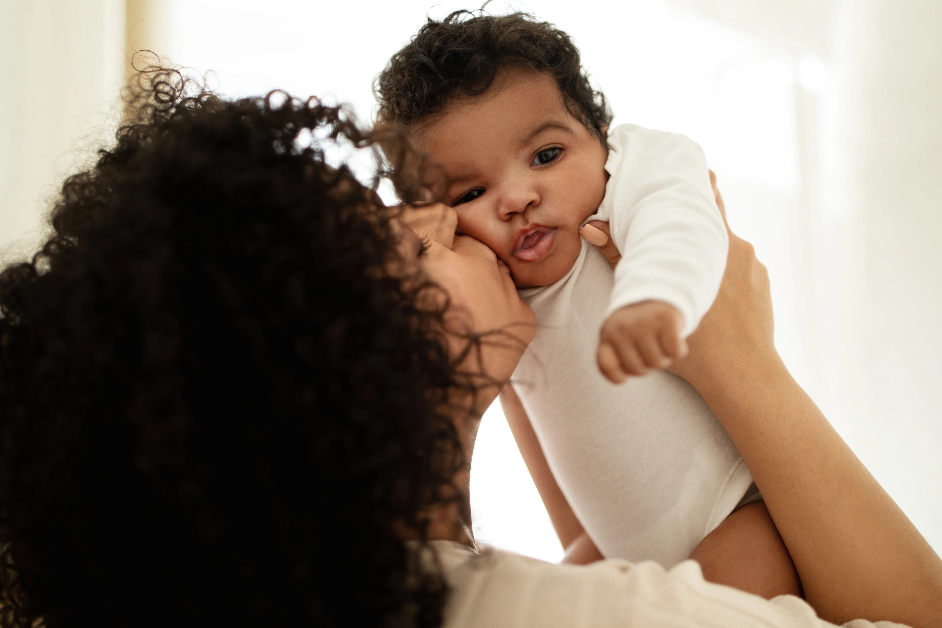 Happy millennial african american mother kissing little child, enjoy relax together, have fun in bedroom interior