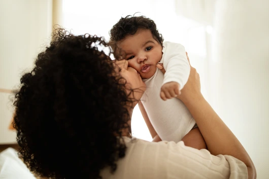Happy millennial african american mother kissing little child, enjoy relax together, have fun in bedroom interior