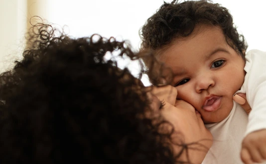 Happy millennial african american mother kissing little child, enjoy relax together, have fun in bedroom interior