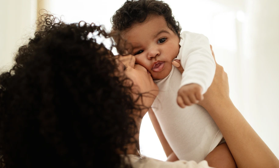 Happy millennial african american mother kissing little child, enjoy relax together, have fun in bedroom interior