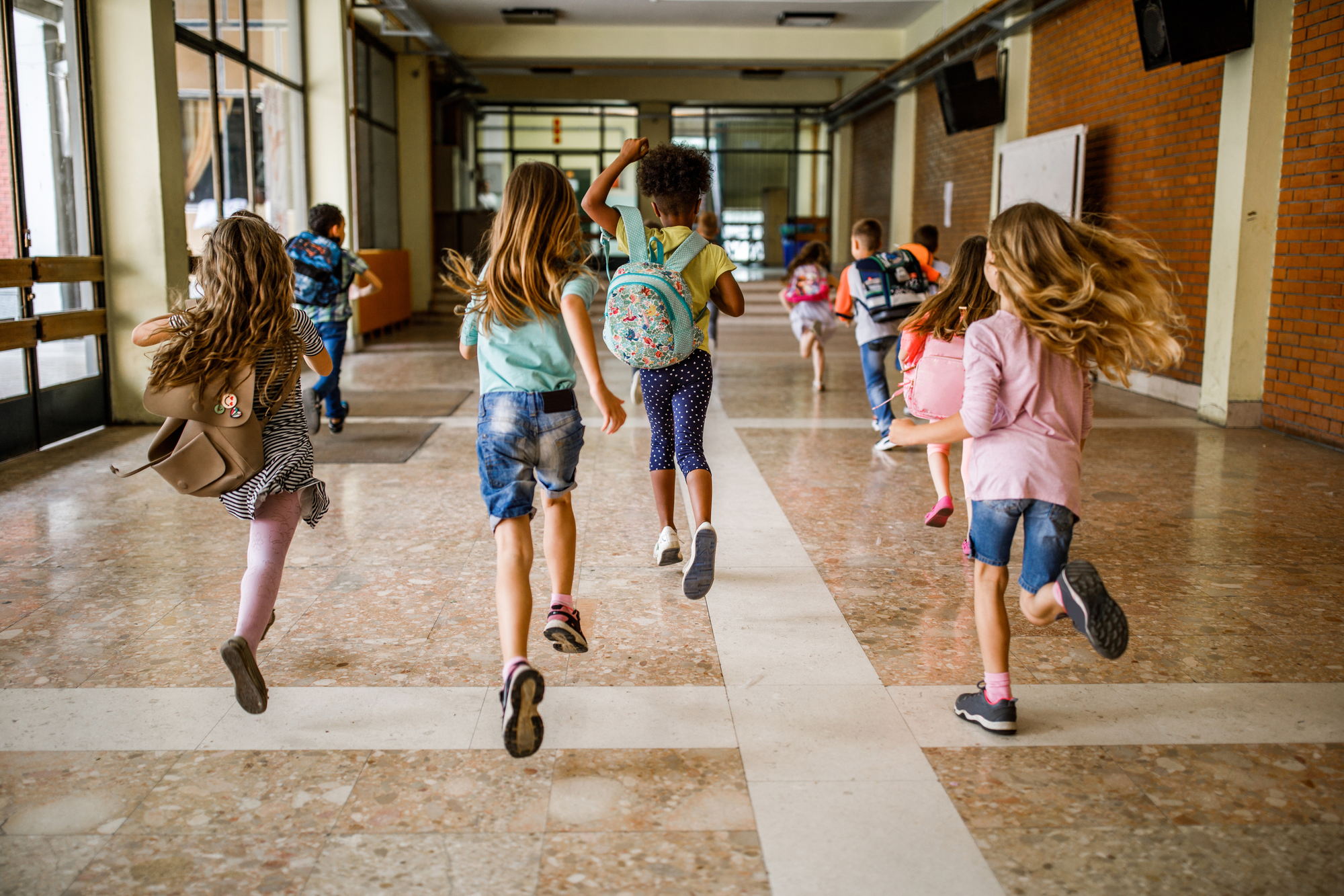 Rear view of group of school children running down the hallway.