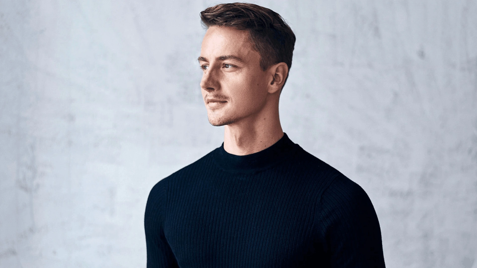 Junger Mann in schwarzem Pullover schaut nach rechts, ruhig lächelnd, PALMBERG