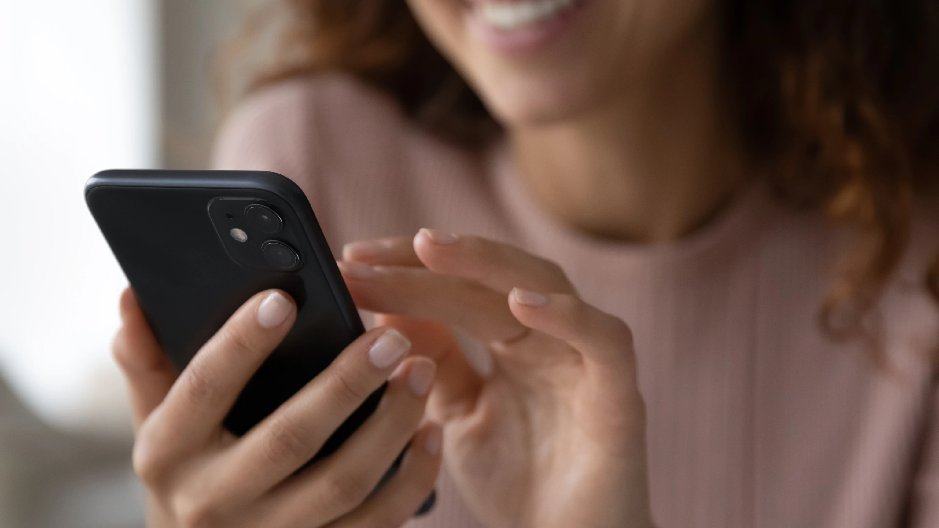 Junge Frau sieht lächelnd auf ihr Smartphone