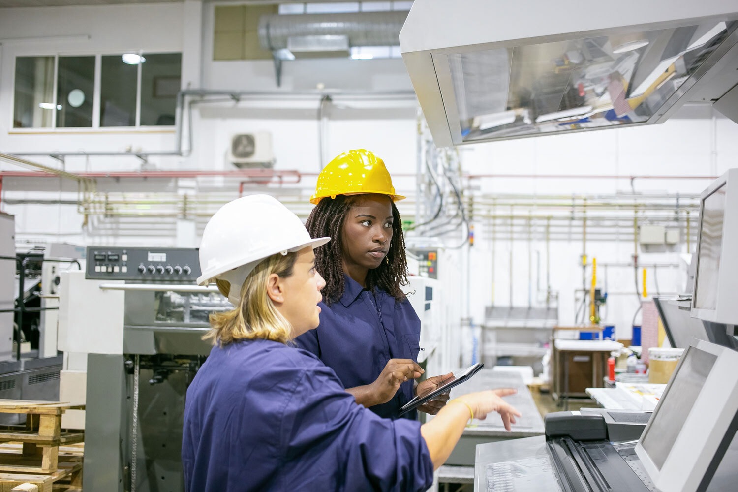 Mentoring auch für Frauen wichtig Ältere erfahrene Arbeitnehmerin erklärt jüngerer Arbeitnehmerin etwas an einer Maschine