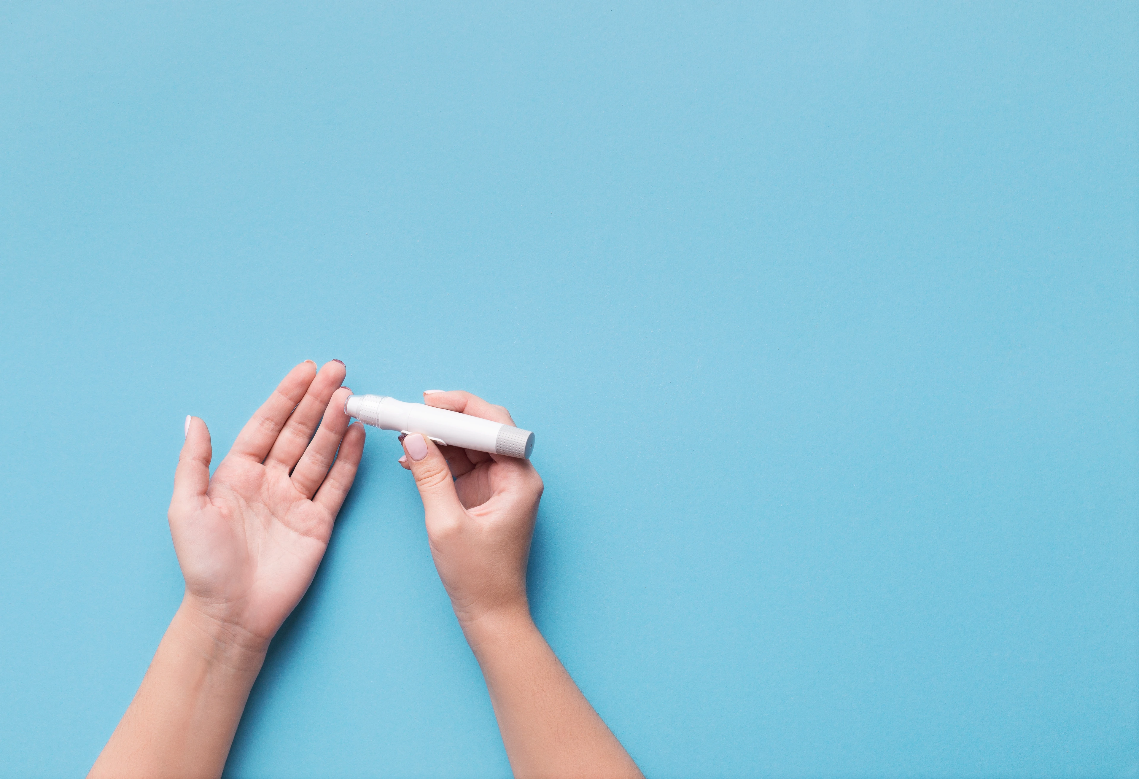 Woman using glucometer on blue background, top view