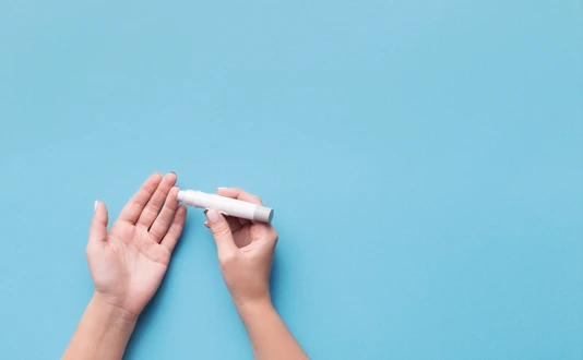Woman using glucometer on blue background, top view