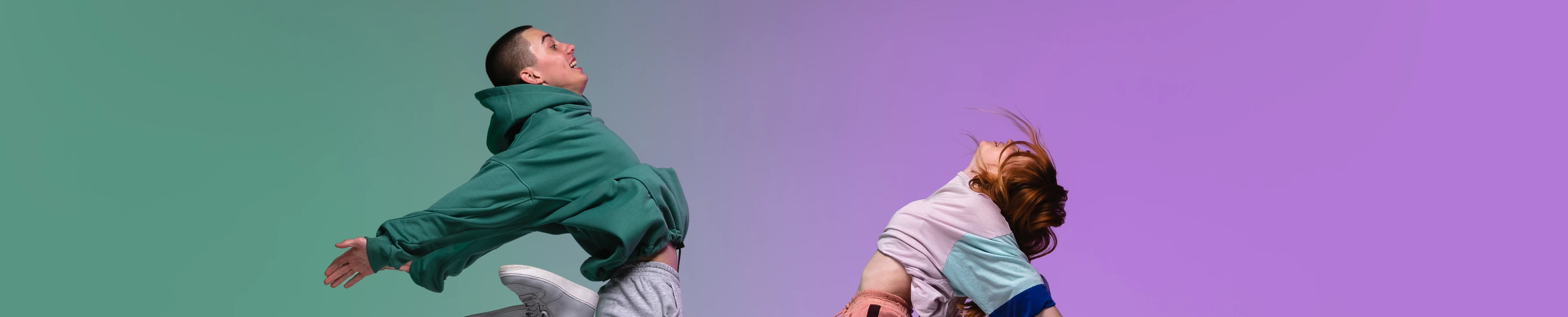 Boy and girl dancing hip-hop in stylish clothes on gradient background at dance hall in neon light.