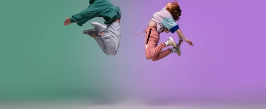 Boy and girl dancing hip-hop in stylish clothes on gradient background at dance hall in neon light.