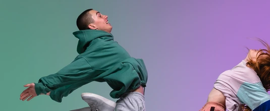 Boy and girl dancing hip-hop in stylish clothes on gradient background at dance hall in neon light.