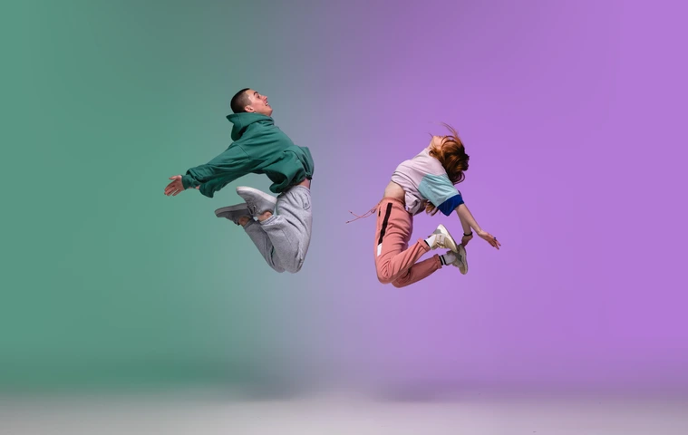 Boy and girl dancing hip-hop in stylish clothes on gradient background at dance hall in neon light.