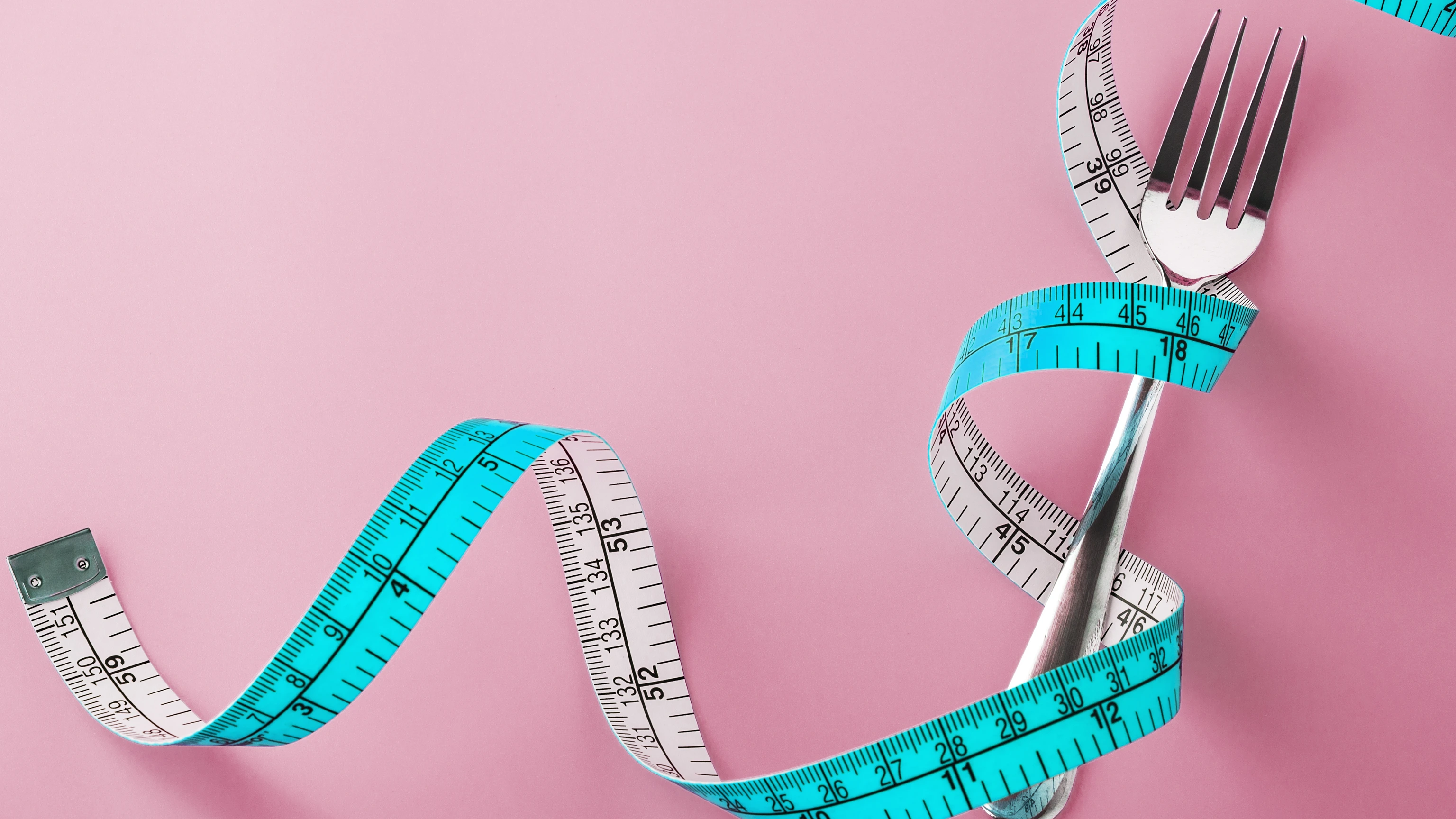 Fork with measuring tape around on pink background