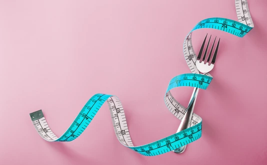 Fork with measuring tape around on pink background