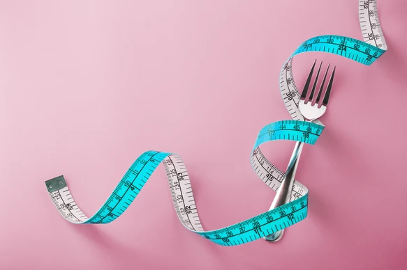 Fork with measuring tape around on pink background
