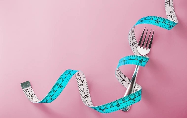 Fork with measuring tape around on pink background
