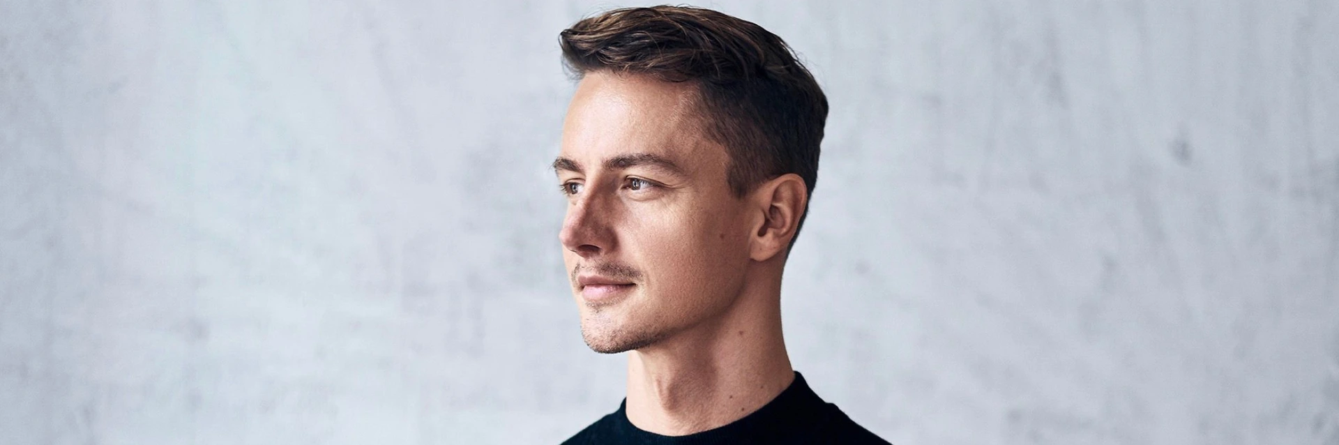 Junger Mann in schwarzem Pullover schaut nach rechts, ruhig lächelnd, PALMBERG