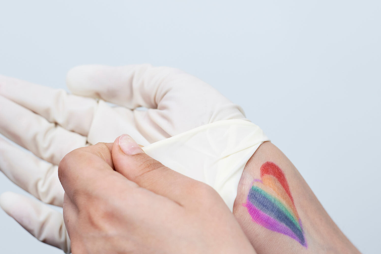 Pflege von queeren Menschen LGBTQ+ Hand mit Handschu und Regenbogenherz