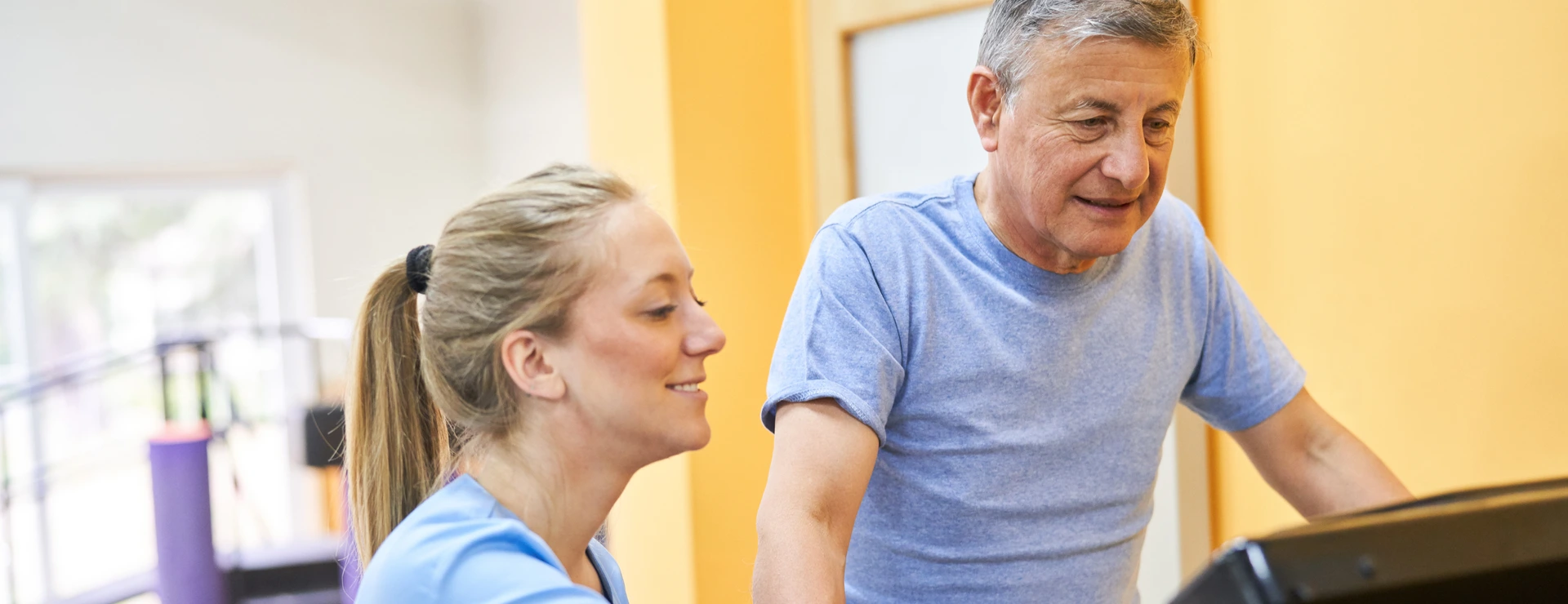 Young physiotherapist assisting senior man on treadmill