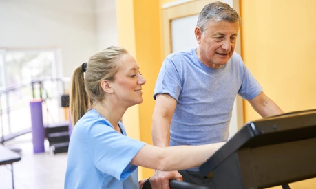 Young physiotherapist assisting senior man on treadmill