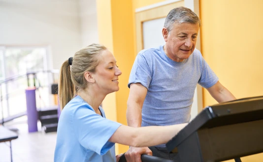 Young physiotherapist assisting senior man on treadmill