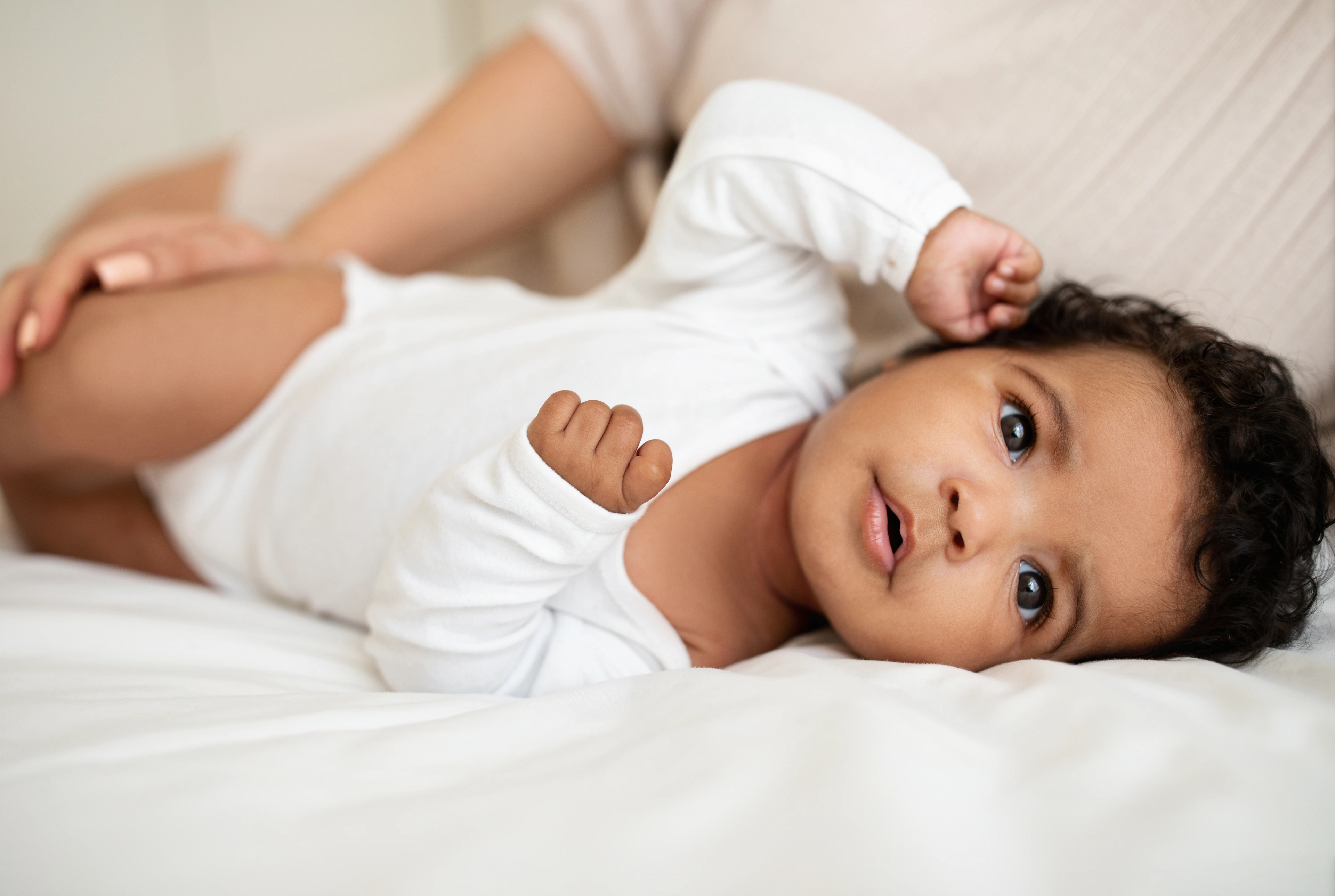 Sweet cute little african american baby lies on soft bed with mom, rest and relax, enjoy free time at home, close up