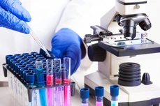 Lab technician working with equipment: tweezers, microscope, test tubes  filled with colored fluid, chemical flasks