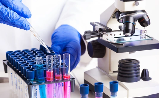 Lab technician working with equipment: tweezers, microscope, test tubes  filled with colored fluid, chemical flasks