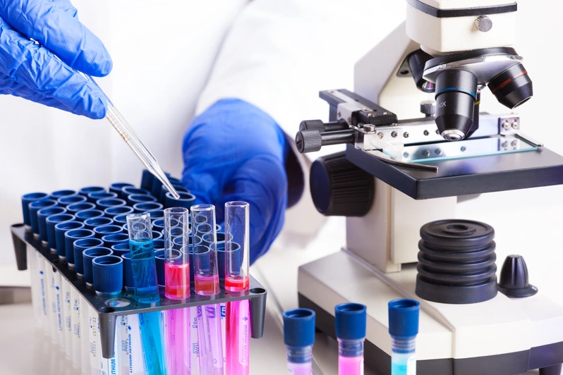 Lab technician working with equipment: tweezers, microscope, test tubes  filled with colored fluid, chemical flasks