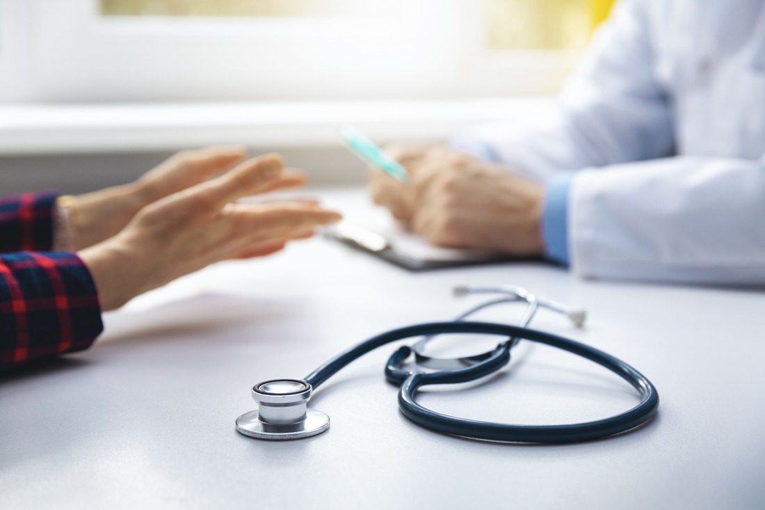 medical consultation - doctor talking to patient in clinic office. focus on stethoscope